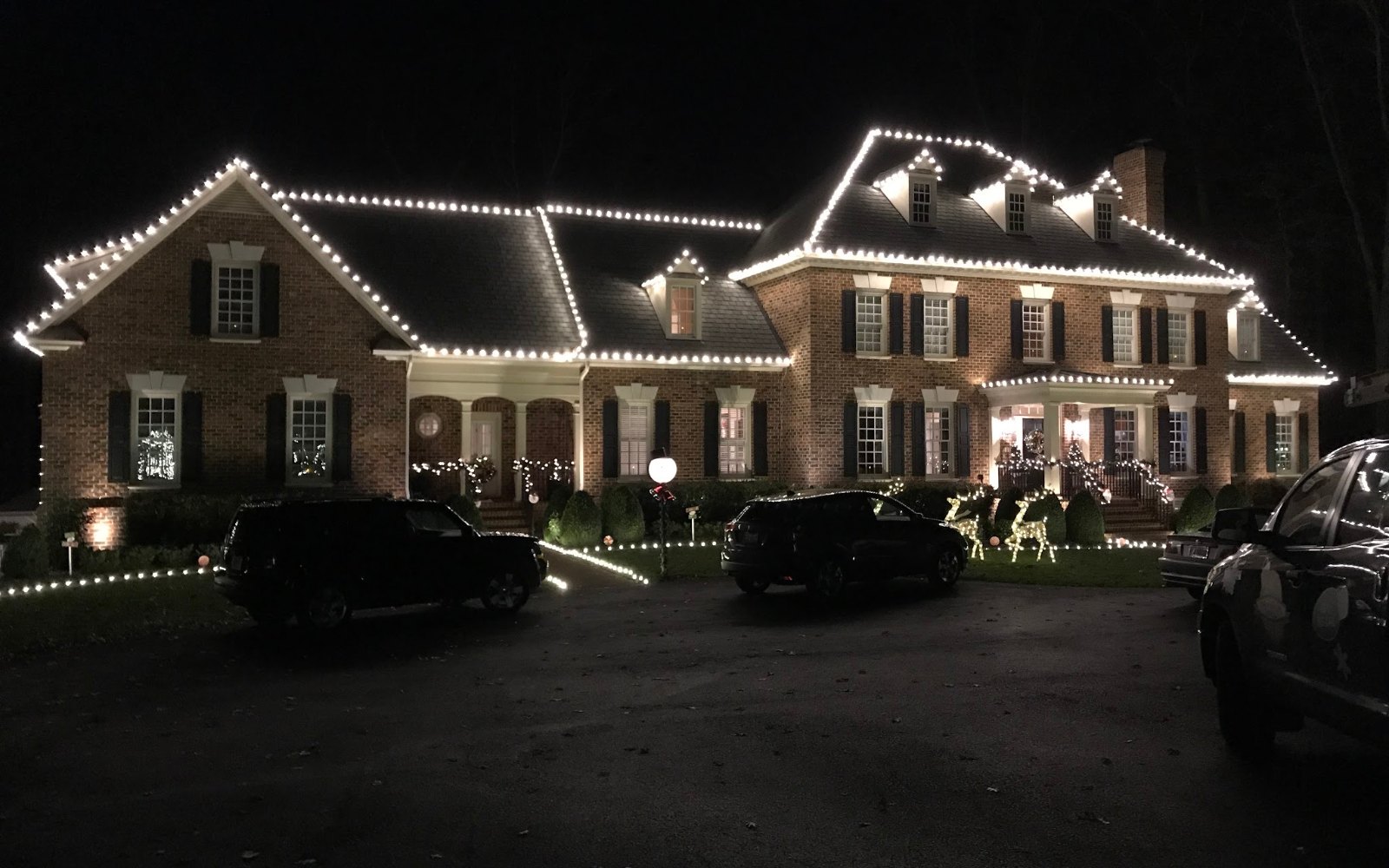 Christmas light installation by Monty's Lighting Co., serving Glen Allen, VA — a brick colonial outlined in warm white, with lit wreaths and a lit front walk